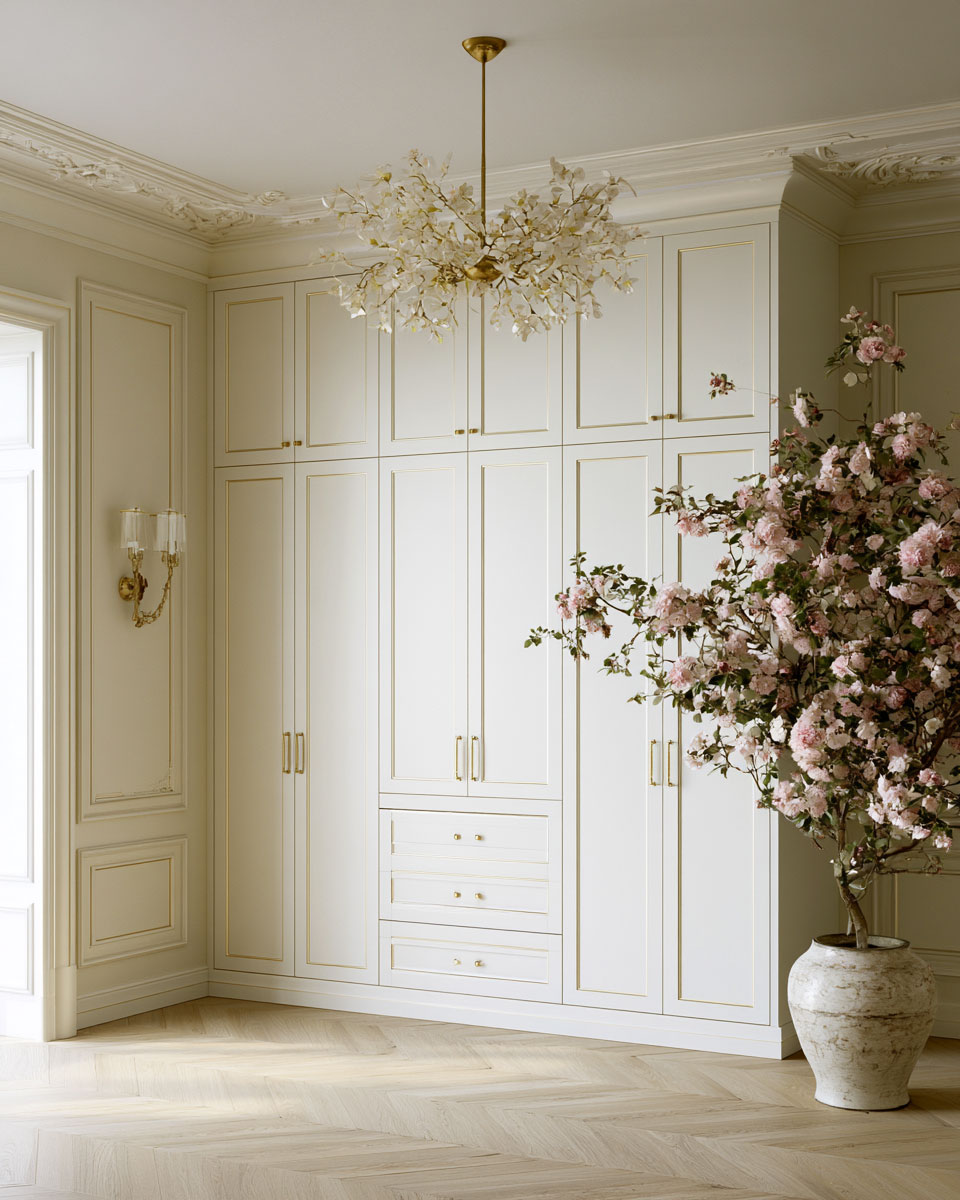 Elegant luxury dressing room with floor-to-ceiling bespoke white wardrobes, gold trim detailing, ornate ceiling moldings, a floral chandelier, herringbone wood flooring, and a large pink flowering tree in a decorative stone planter.