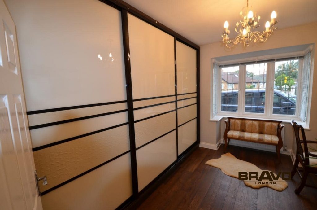 A modern room with large black sliding door wardrobes, glossy wooden floors, a classic chandelier, a wooden bench with a patterned cushion, and a small rug by the balcony window.