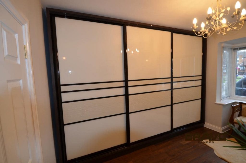 A large, elegant sliding door with a black frame and multiple frosted glass panels, installed in a room with light brown walls and bespoke furniture.
