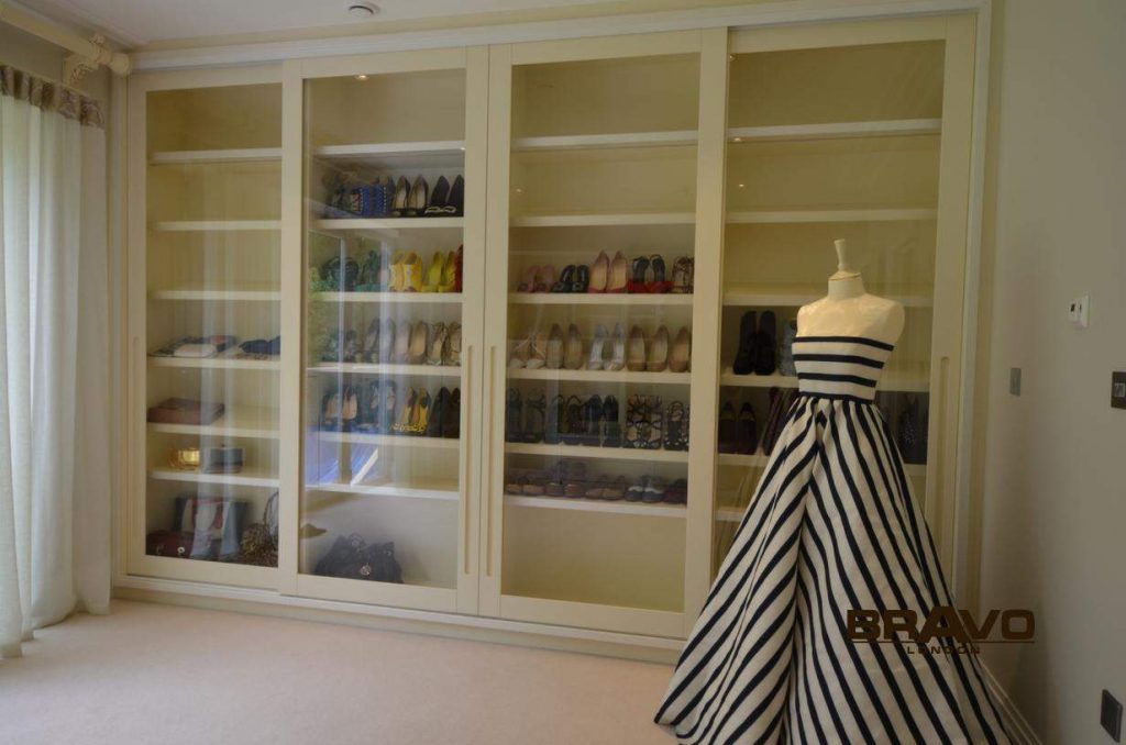 A spacious walk-in closet featuring a white built-in shelving unit filled with neatly organized shoes and a mannequin dressed in a black and white striped dress, complemented by fitted wardrobes along the adjacent wall.