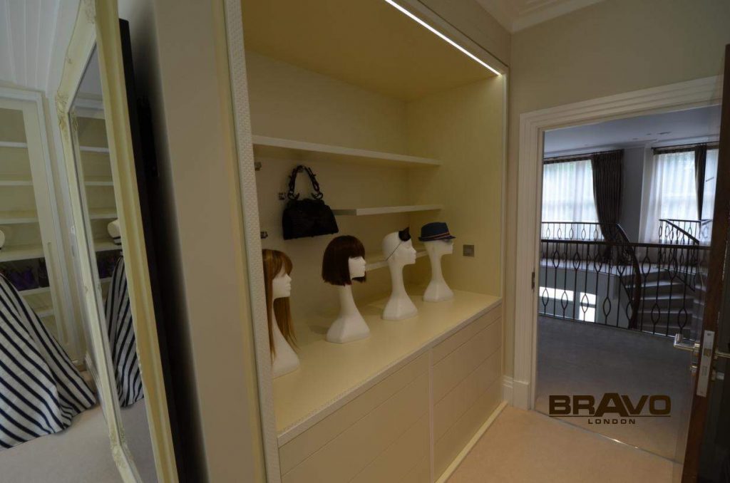 A stylish walk-in closet featuring a lit alcove with four mannequin heads displaying wigs, adjacent to sliding door wardrobes overlooking a lower floor.