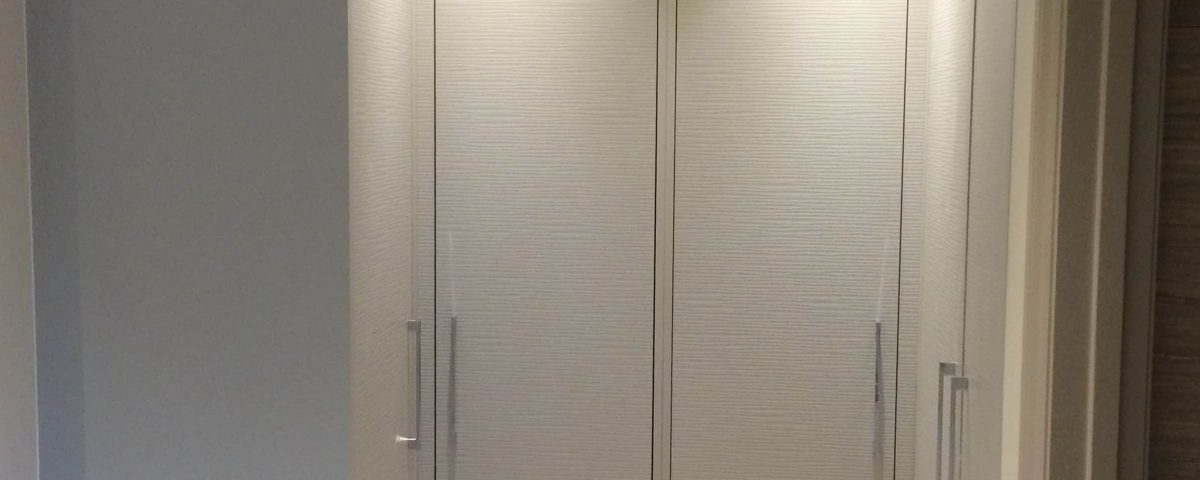 A pair of closed, modern hinged doors in a light beige color set within a softly lit room, featuring sleek metal handles.