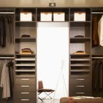 A spacious walk-in wardrobe with shelves, drawers, and hanging spaces filled with clothing and accessories, well-lit by overhead lights and a bright central opening.