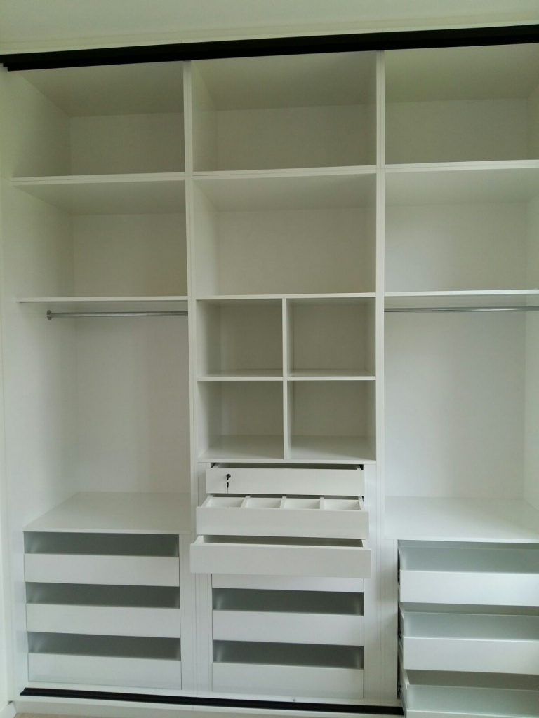 A spacious, white 3 m high wardrobe in Edgware, London, with multiple shelves, drawers, and two clothes hanging rods. The unit has open storage spaces for organization, including a set of small square shelves in the center and several drawers with horizontal handles.