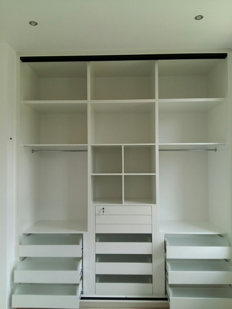 A white, built-in wardrobe standing 3 meters high with multiple shelves, a hanging rod, and drawers. The unit features open compartments on the top and sides, two sets of drawers at the bottom, and one central vertical drawer section with smaller compartments above it. Perfect for any London or Edgware home.
