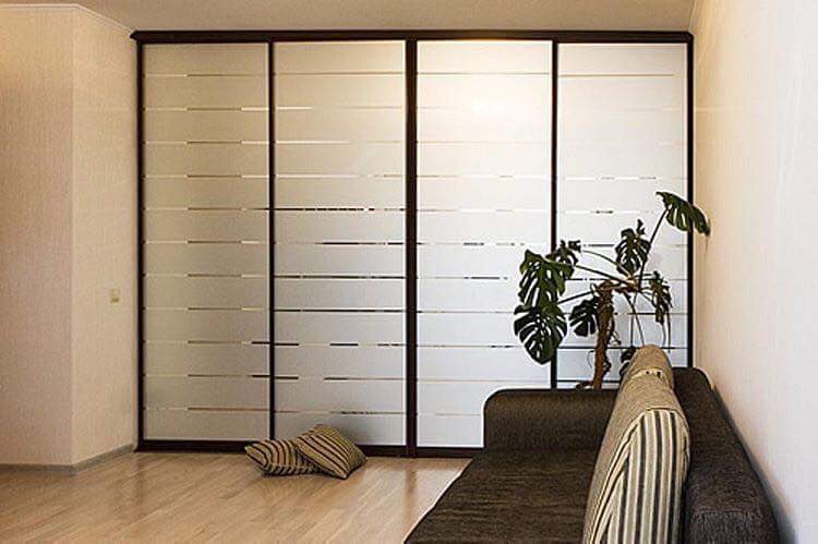 A modern living room with a large fitted wardrobes closet with white panels, a brown couch to the right, and a green potted plant in the corner.