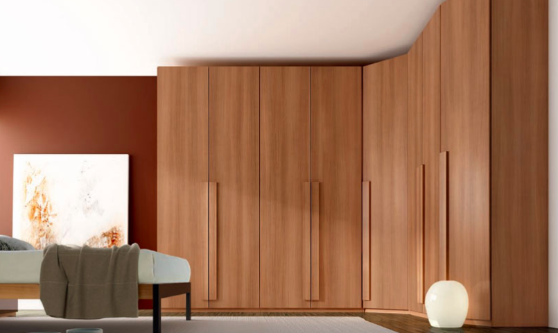 A bedroom with a large wooden wardrobe covering one wall serves as a perfect storage solution. The room features a white bed with a gray blanket, a modern round light on the floor, a large abstract painting, and red accent walls. Bright natural light streams in from a large window on the left.