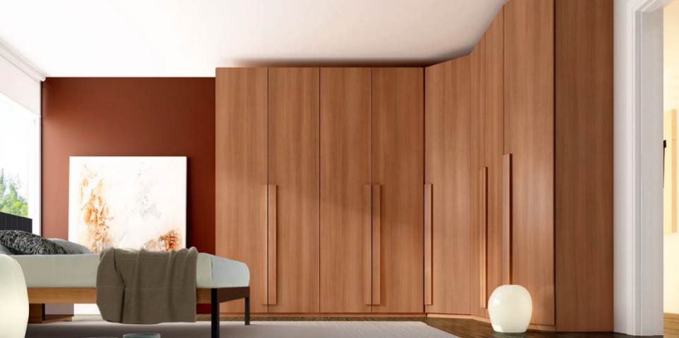 A bedroom with a large wooden wardrobe covering one wall serves as a perfect storage solution. The room features a white bed with a gray blanket, a modern round light on the floor, a large abstract painting, and red accent walls. Bright natural light streams in from a large window on the left.