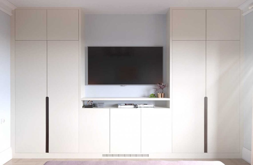 A minimalist room features a large flat-screen TV mounted on a light gray wall. Below the TV, a shelf houses some books and a small plant. Flanking the TV are two tall, sleek white cabinets with simple, modern design and black vertical handles, creating cozy alcoves for added visual interest.
