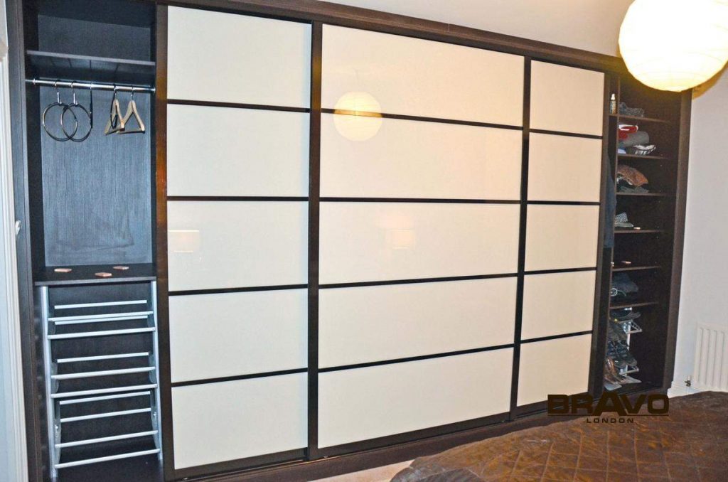 A modern walk-in wardrobe with large sliding doors featuring a stylish black and white design. The interior is equipped with shelving filled with various clothing items.