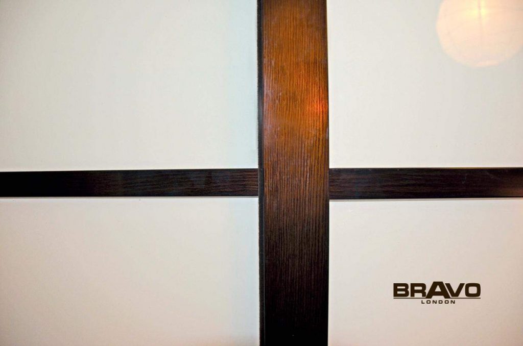 A close-up of a bespoke wooden cross design on a wall with the word "bravo london" in bold at the bottom right corner.