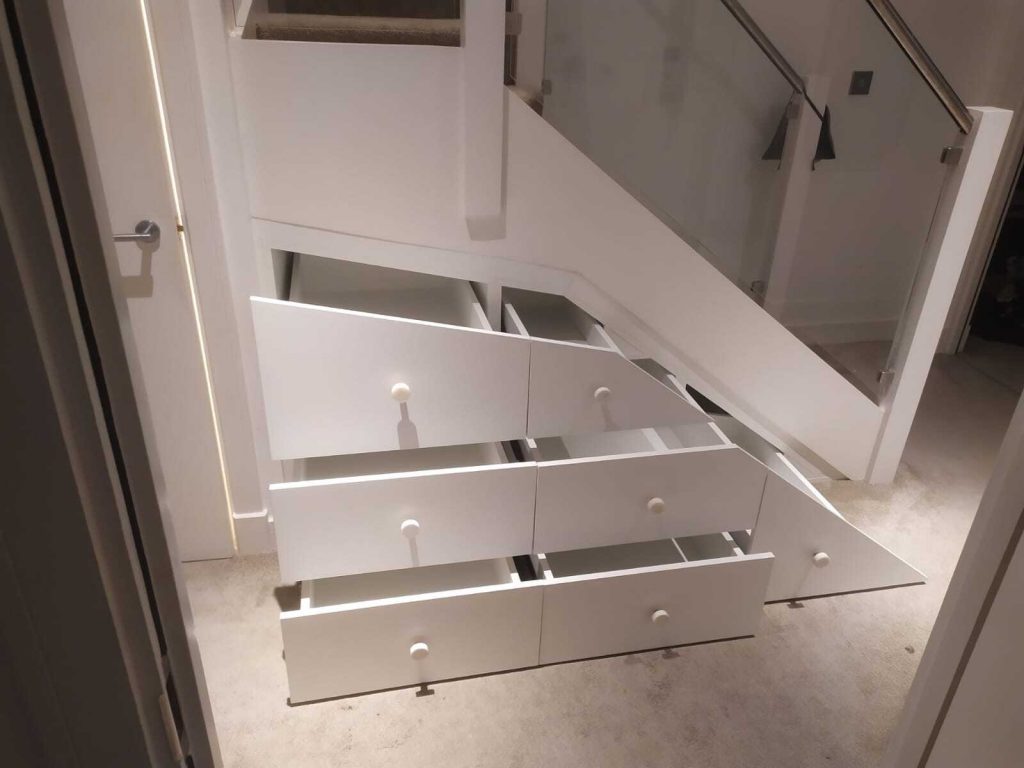 Staircase with built-in white storage drawers in a modern home interior, showcasing an innovative design that efficiently utilizes space under the stairs with bespoke furniture.