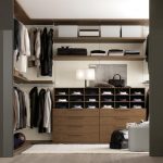 A modern, well-organized walk-in closet featuring bespoke furniture with wooden shelves filled with neatly arranged clothes, shoes, and accessories, ambient lighting, and a cozy rug.