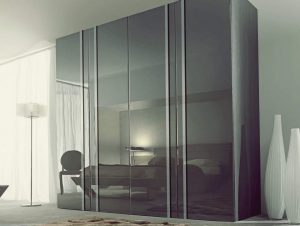 Modern bedroom with sliding door wardrobes reflecting a bed and minimalist decor, featuring muted tones, a floor lamp, and tall decorative vases.