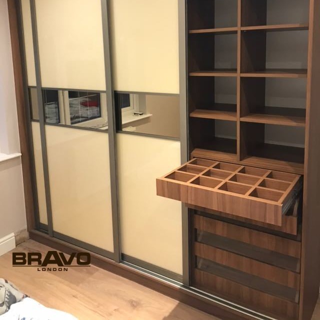 A modern fitted wardrobe with frosted glass panels, featuring an open section with shelving and a built-in drawer unit with a wooden compartment organizer.