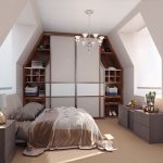 An attic bedroom with slanted ceilings featuring a built-in wardrobe with sliding door wardrobes, a cozy bed with beige bedding, grey side cabinets, a lamp, and a chandelier. Two windows provide natural light.