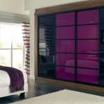 Modern bedroom with a large bed, white and purple bedding, and floor-to-ceiling sliding door wardrobes in reflective purple. The room features minimalist decor, a large window, and a neutral color palette.
