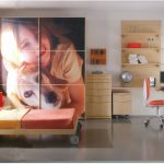 A modern office space featuring bespoke wooden furniture, including a desk and shelving units, with a large wall-sized print of a smiling woman and a dog as the focal point.