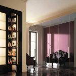 Elegant interior with open black french doors revealing a sliding door wardrobe. The adjacent room features ornate black furniture with pink walls, lit by natural sunlight.