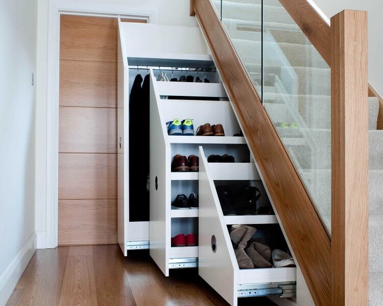A modern staircase with a glass and wood banister features built-in storage drawers underneath. The drawers, reminiscent of fitted furniture, are pulled out to reveal shelves for clothes, shoes, and other items, maximizing space. This sleek and efficient design is perfect for fitted wardrobes in London homes.