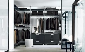 A modern, well-organized walk-in closet with an array of neatly hung clothes, shelves with accessories, and a central island with drawers. The closet features reflective surfaces, soft lighting, and sliding door wardrobes.