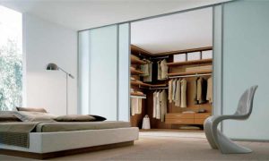 Modern bedroom with a large bed, an abstract chair, and open hinged door wardrobes revealing a spacious, organized wardrobe with various clothes and accessories.