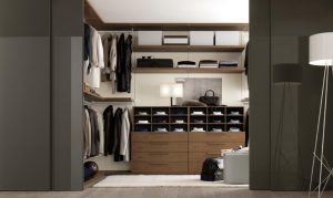 A modern, well-organized walk-in wardrobe featuring wooden shelves and drawers filled with clothes, shoes, and bags, showcased under warm lighting.