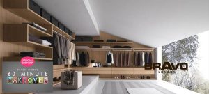 A modern and spacious walk-in wardrobe with wooden shelves and cabinets, displaying an assortment of neatly organized clothes and accessories. The left side shows a window with a view of trees.