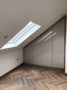 A corner wardrobe for storing clothes in a room with sloped ceiling and a roof light window.