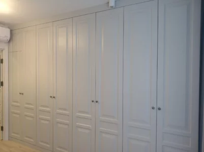 Grey traditional hinged doors on a carcass forming a fitted wardrobe in a bedroom. 