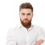 A man with a thick beard and short hair stands against a plain white background. He is wearing a white dress shirt, his arms crossed, giving a serious and confident expression—much like the tailored craftsmanship seen in fitted wardrobes in London.