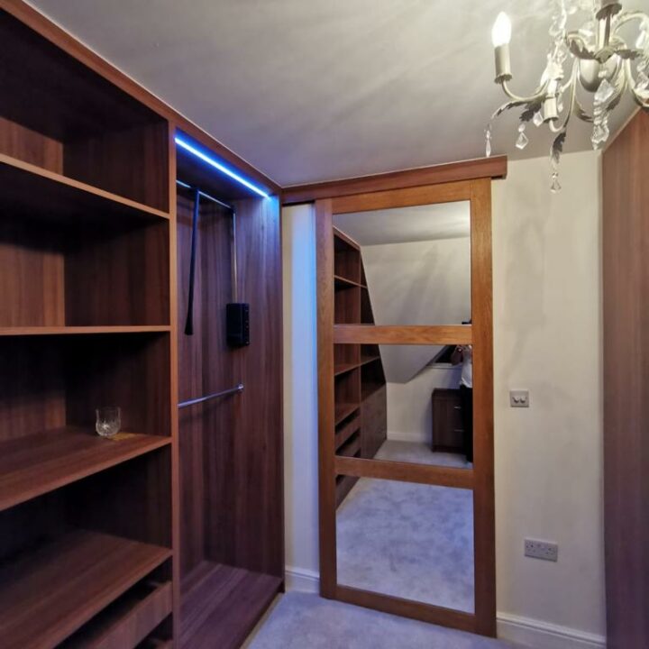 A cozy room featuring an open sliding door leading to a spiral staircase, with a built-in shelf on the left and a chandelier above. Soft lighting enhances the ambiance.