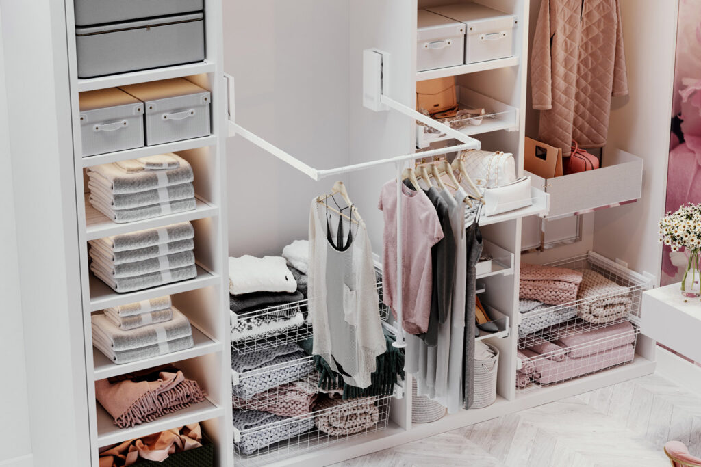 A well-organized walk-in closet with neatly arranged clothes on hangers, stacks of towels, and various storage boxes in a light, modern decor with sliding door wardrobes.