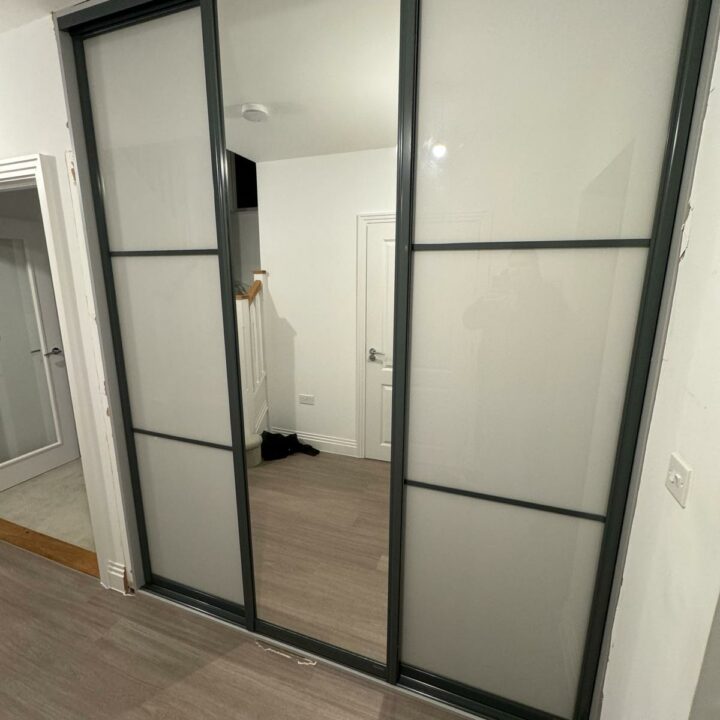 A modern room with sliding door wardrobes on a closet reflecting an interior hallway. Shoes are visible on the floor near the entrance of a white door.