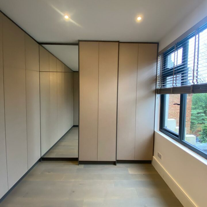 A modern hallway with light gray flooring, large windows, and built-in beige cupboards along one side features custom bespoke furniture. The area is well-lit with ceiling spotlights.