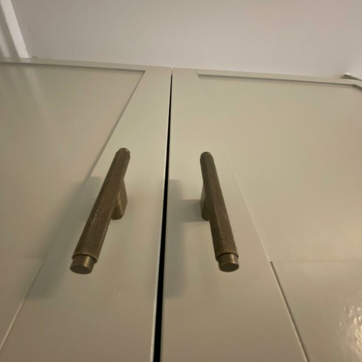 Two golden metallic door handles installed on a white "His and Hers" fitted wardrobe, viewed from above, creating a symmetrical appearance on the surface.