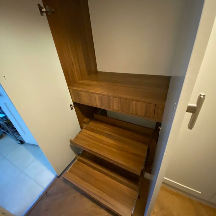 A wooden staircase inside a home, viewed from the top, with the door open revealing a room below equipped with His and Hers fitted wardrobes. The stairs are compact and appear to utilize space efficiently